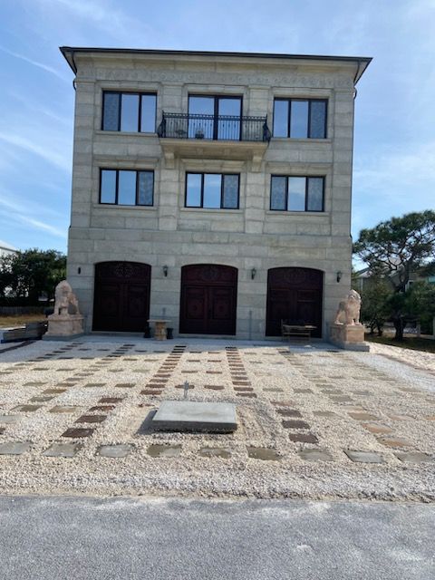 Three-story beige stone building with three arched garage doors and lion statues; gravel driveway.