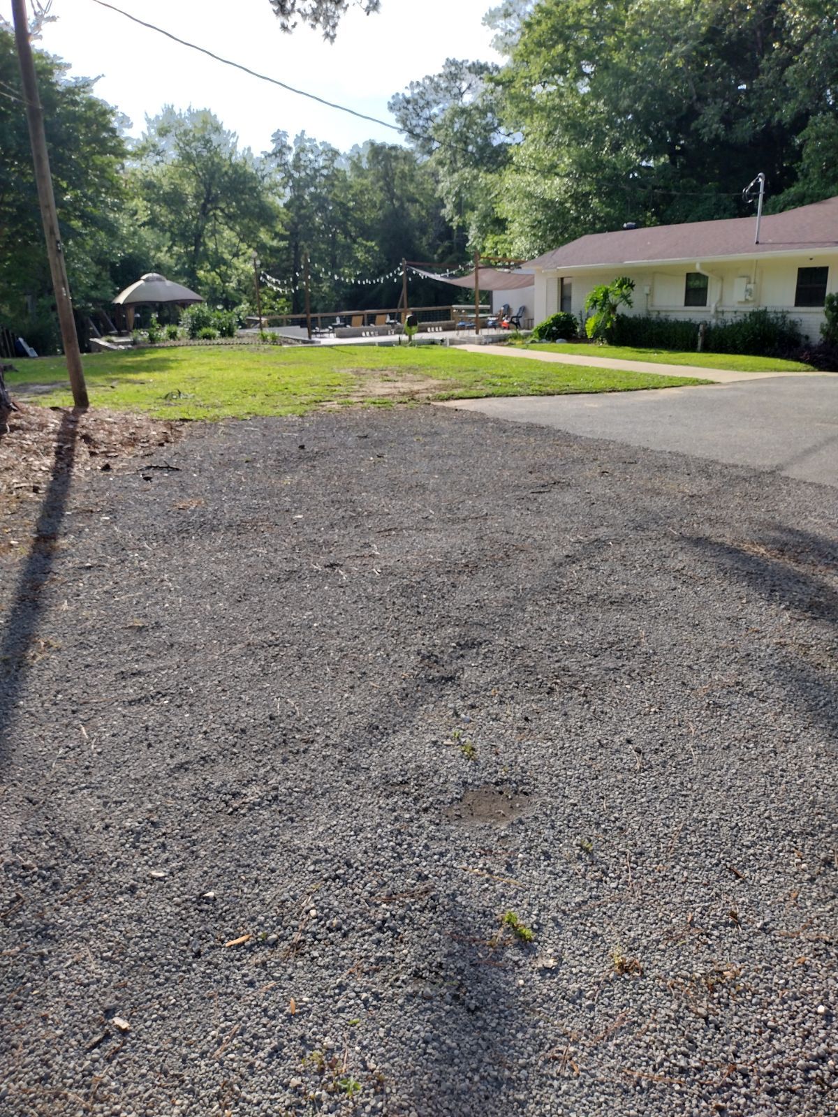Gravel driveway leading towards a grassy area and a white building with a yard.