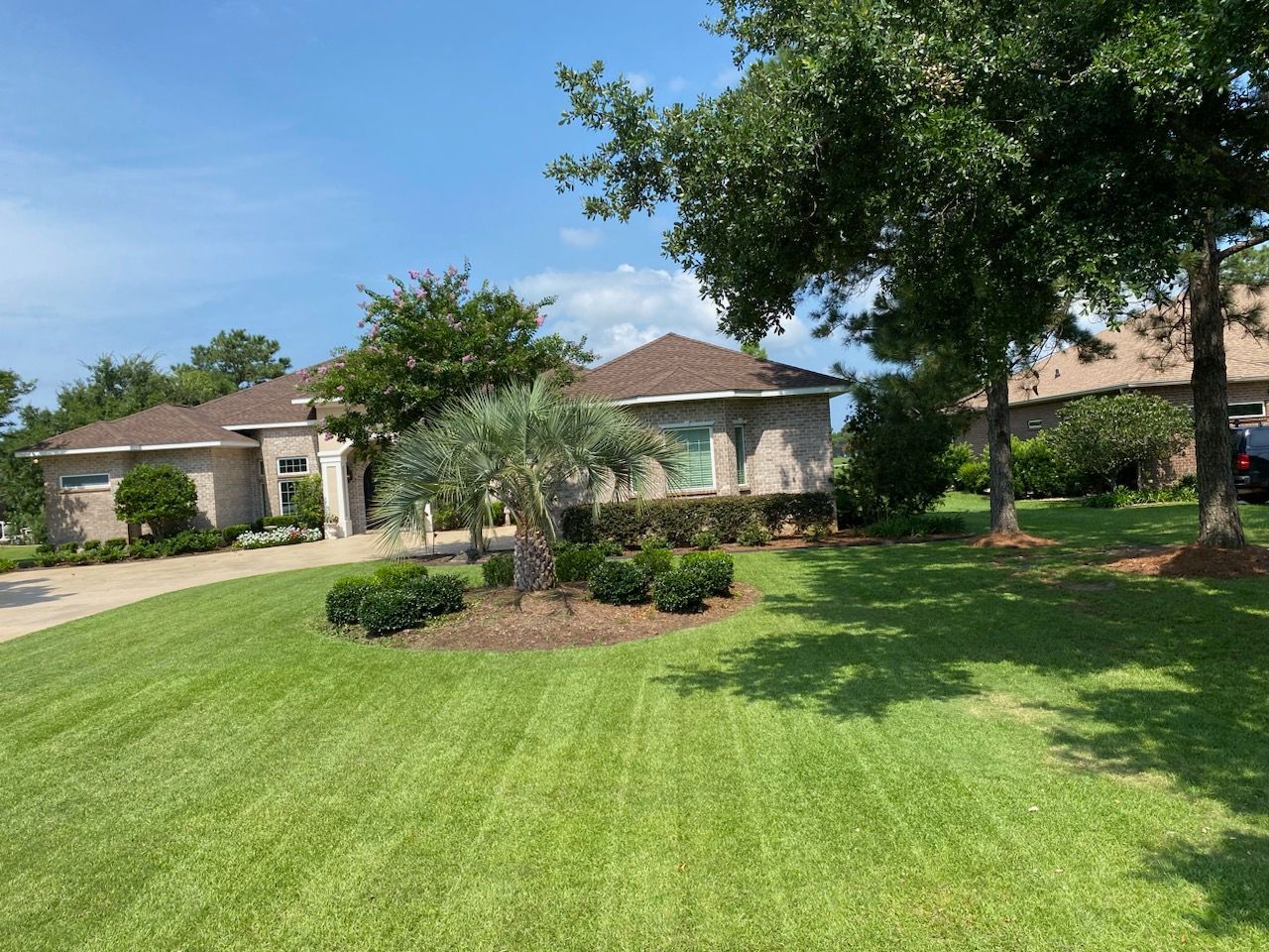 A house with brown roof and tan brick, green lawn, palm tree in front. Sunny day.