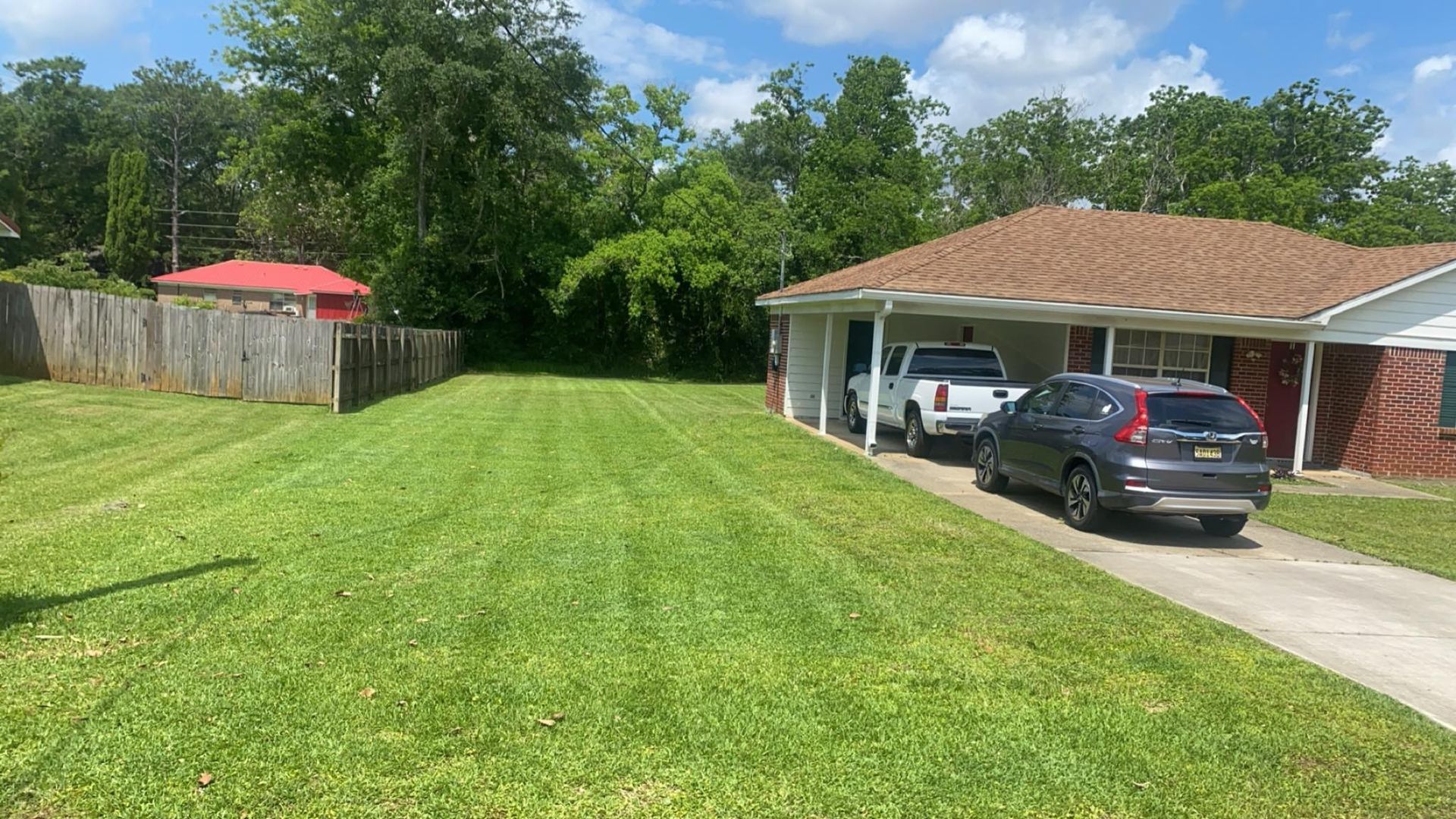 Green lawn leads to a brick house with a covered car port. A white truck and gray SUV are parked.