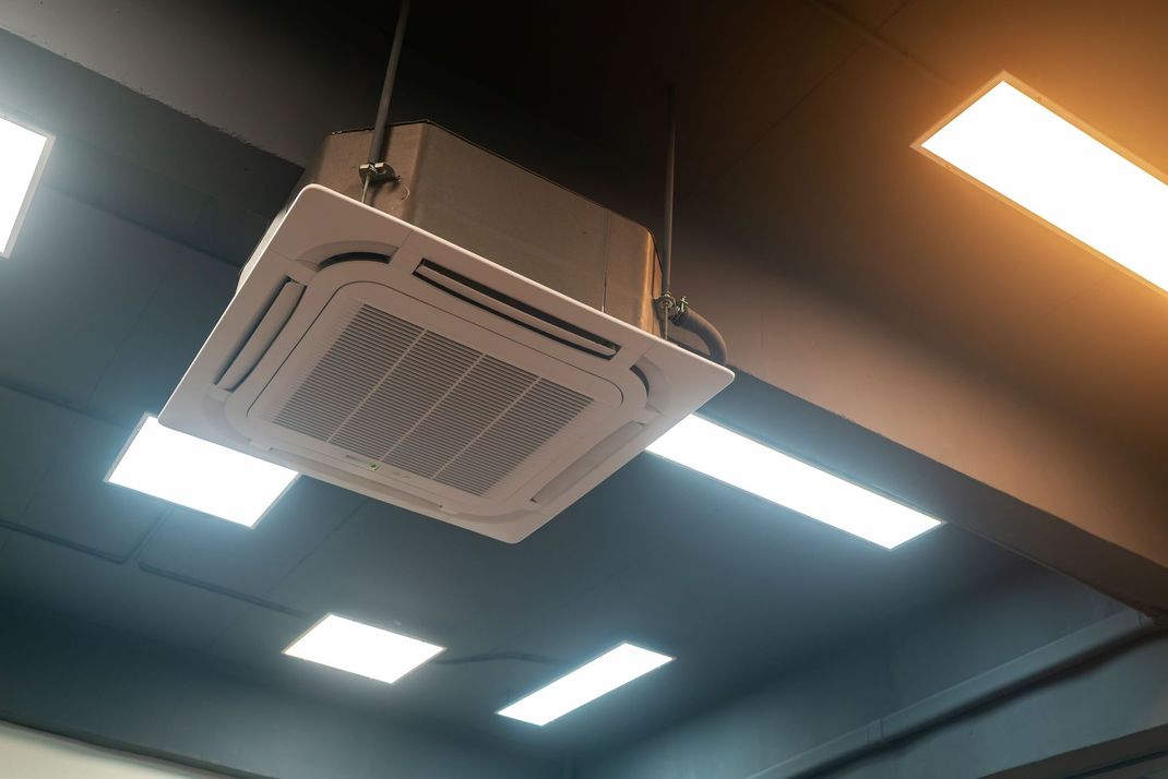 Ceiling-mounted white HVAC unit in an office with bright rectangular ceiling lights.