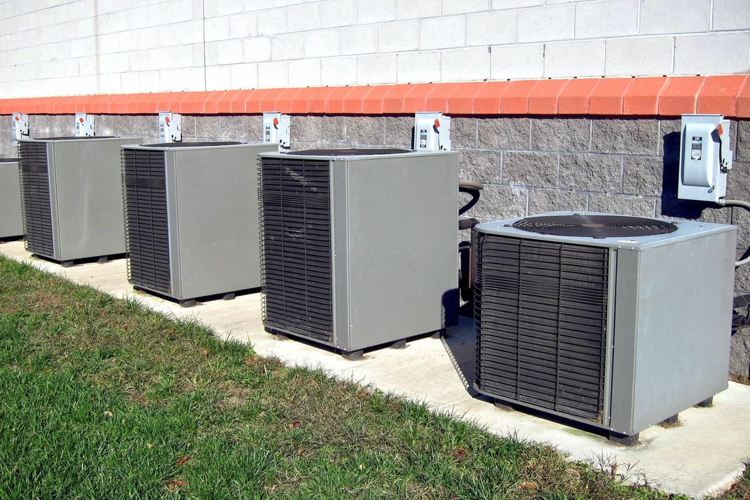 Row of outdoor air conditioning units beside a white brick building with orange trim