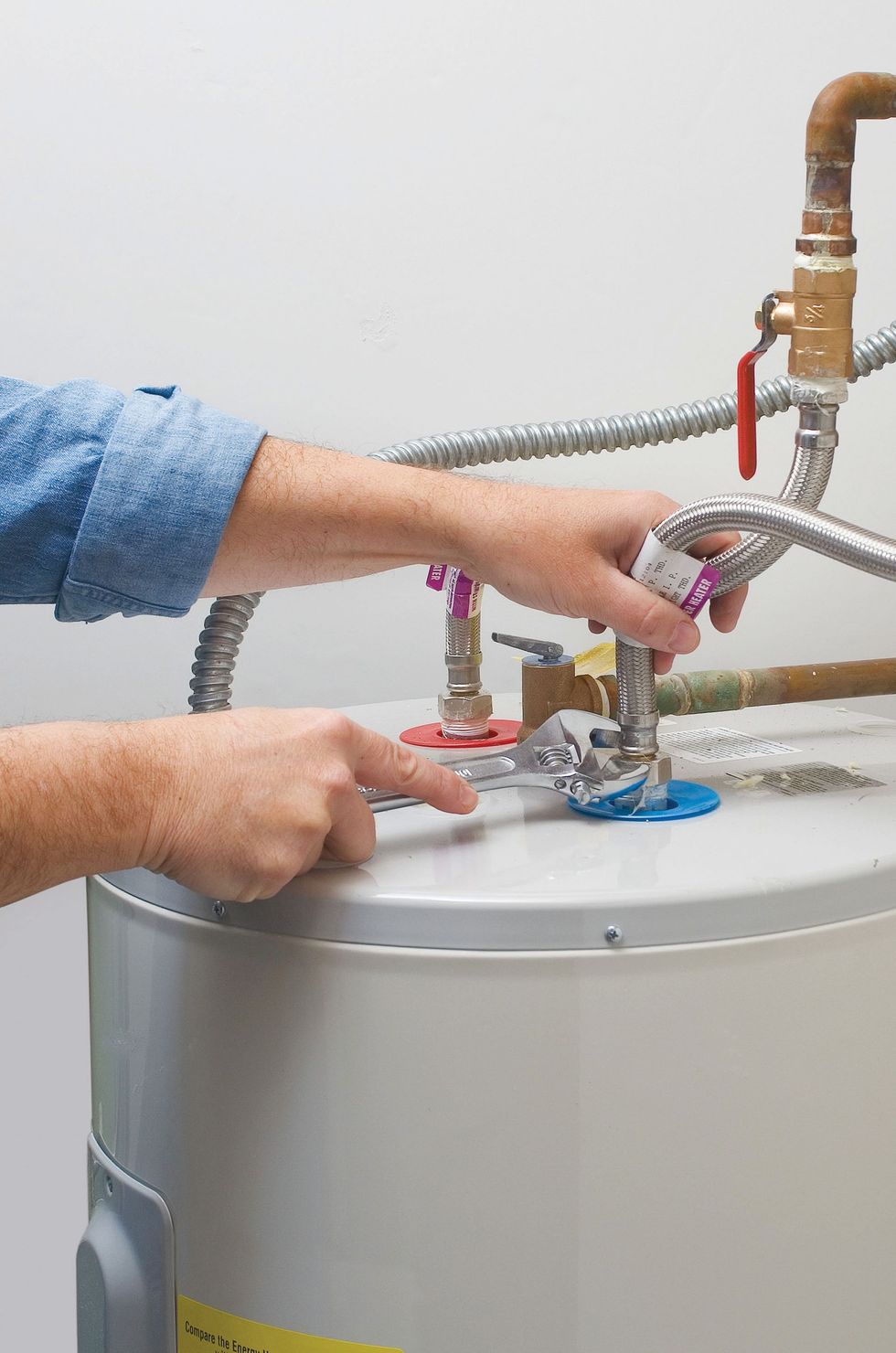 Hands adjusting a faucet on top of a water heater with pipes and a blue scrub pad.
