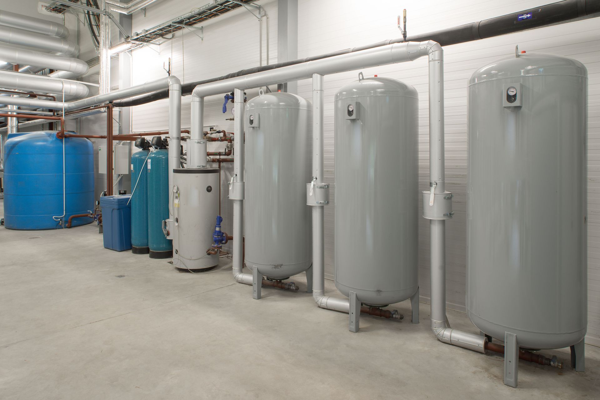 Industrial room with large blue and gray storage tanks, pipes, and concrete floor
