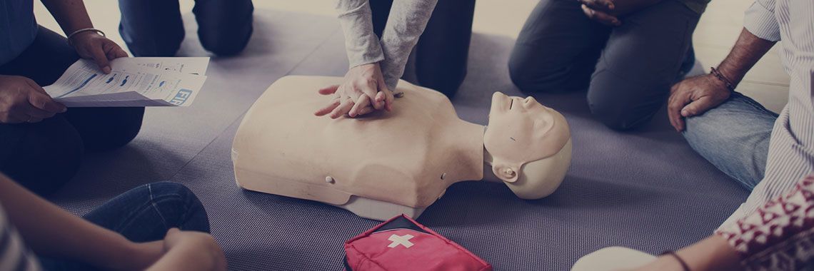 A group of people are sitting around a mannequin on the floor.