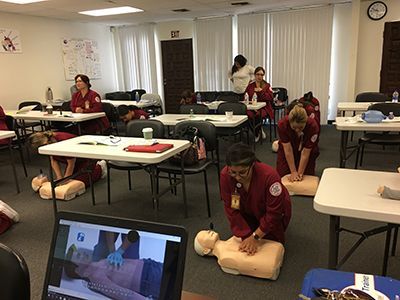 A group of people are practicing a cpr on a mannequin in a classroom.