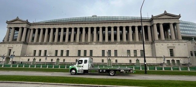 A white flatbed truck parked in front of the grand, columned Field Museum in Chicago on an overcast day.