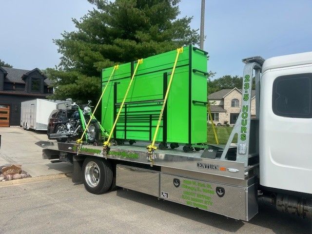 A bright green Snap-on tool chest and a motorcycle are strapped onto the flatbed of a tow truck in a suburban driveway.