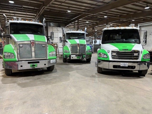 Three white and green semi-trucks parked inside a warehouse facility.