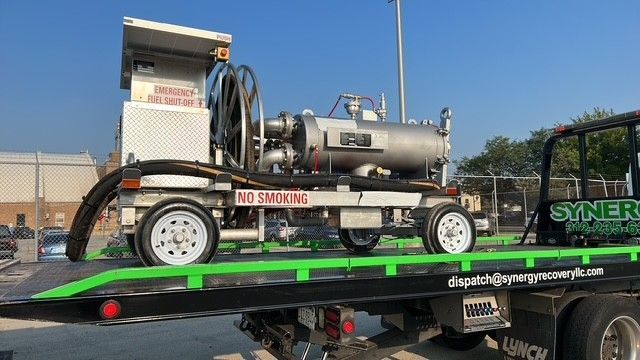 A piece of industrial equipment, featuring a large cylindrical tank, secured on the back of a flatbed tow truck.