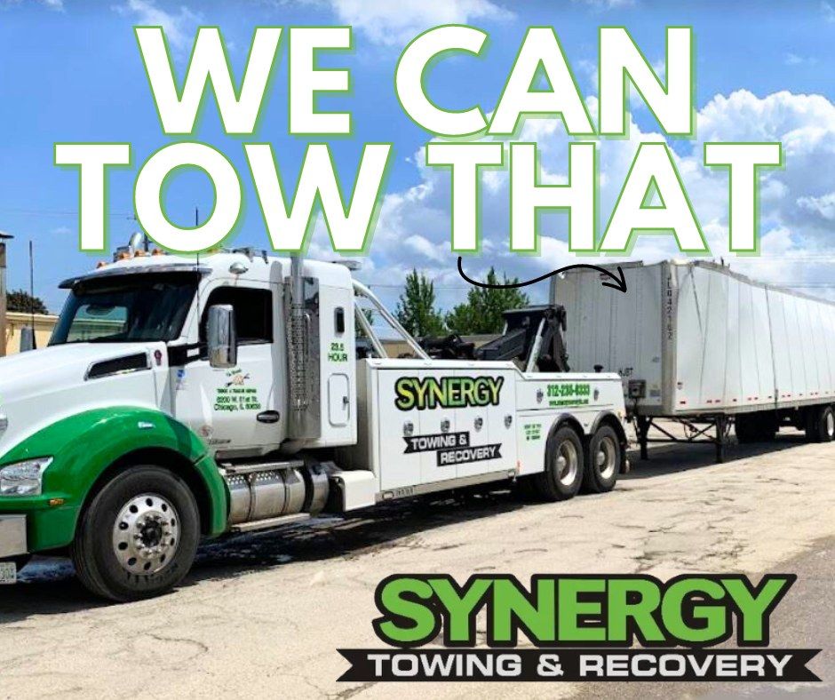 White and green tow truck towing a large white trailer. 