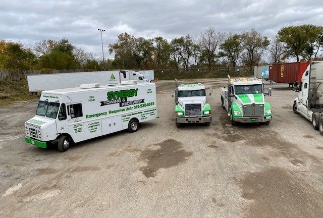 Three white service and tow trucks with green accents parked in an outdoor gravel lot.