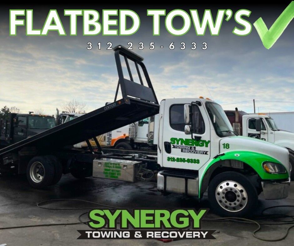 Flatbed tow truck with the Synergy Towing & Recovery logo, green accents, and a phone number.