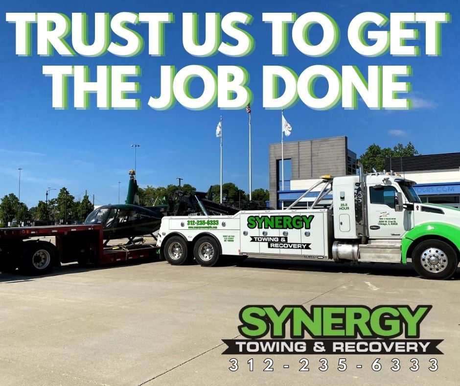 Synergy Towing truck with a car on a trailer under a blue sky.  Text: 