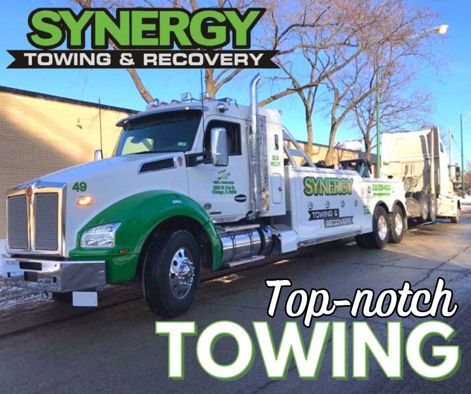 White and green Synergy Towing truck towing another truck. 