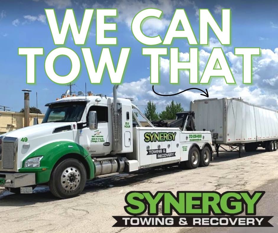 A white and green tow truck towing a large white trailer with the text 