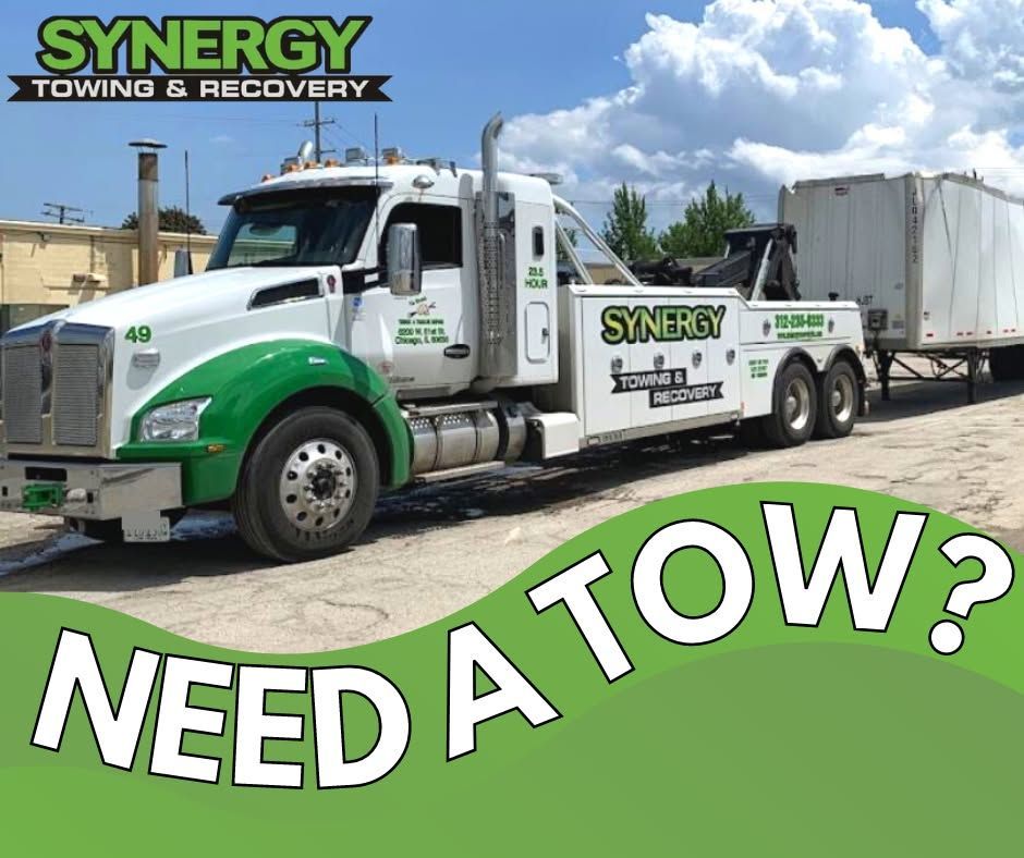 White and green Synergy Towing truck towing a trailer on a gravel road; 