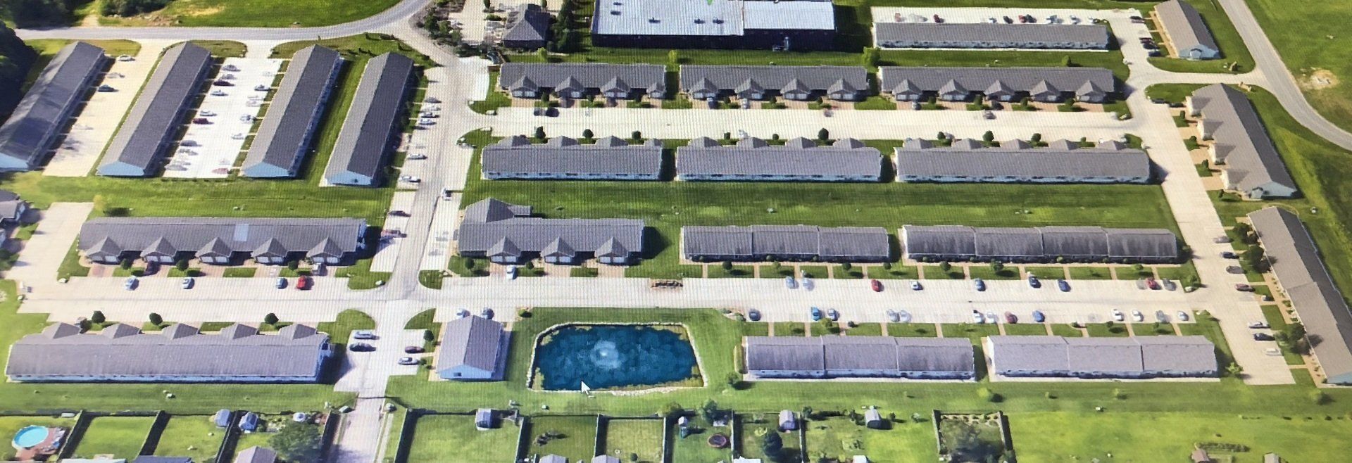 Aerial view of a suburban apartment complex with rows of gray-roofed buildings, parking lots, and green lawns