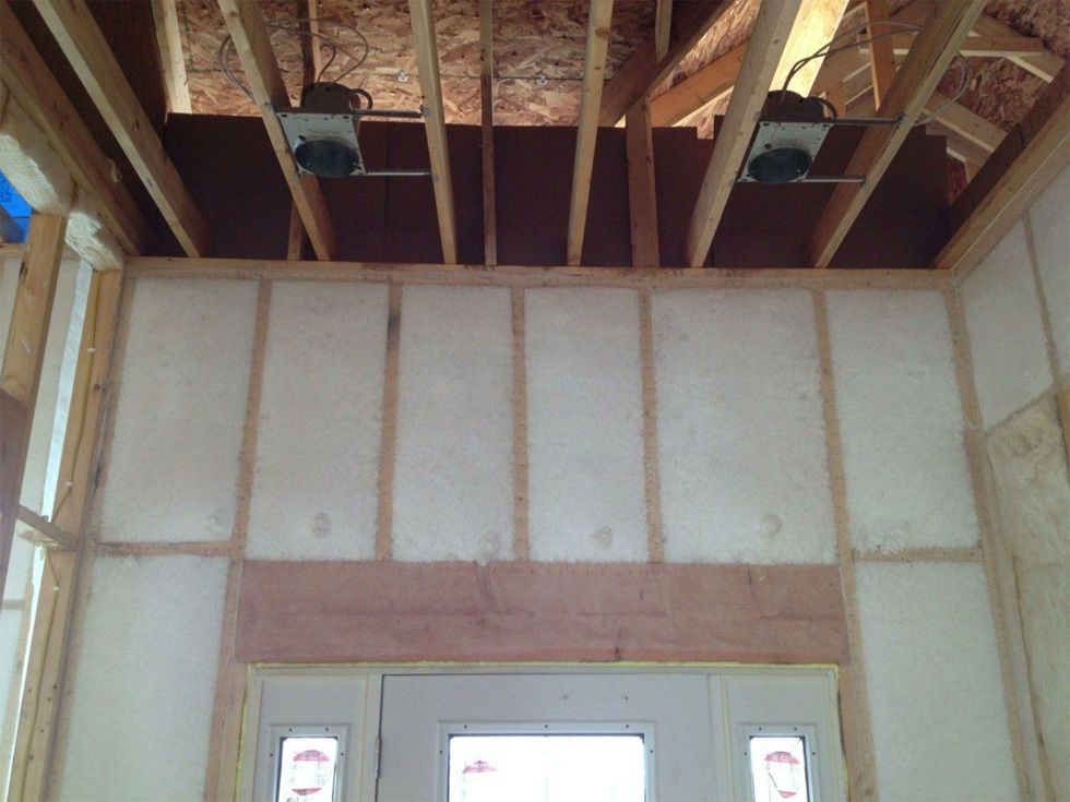 Interior wall under construction with exposed ceiling joists and a white-framed door opening.