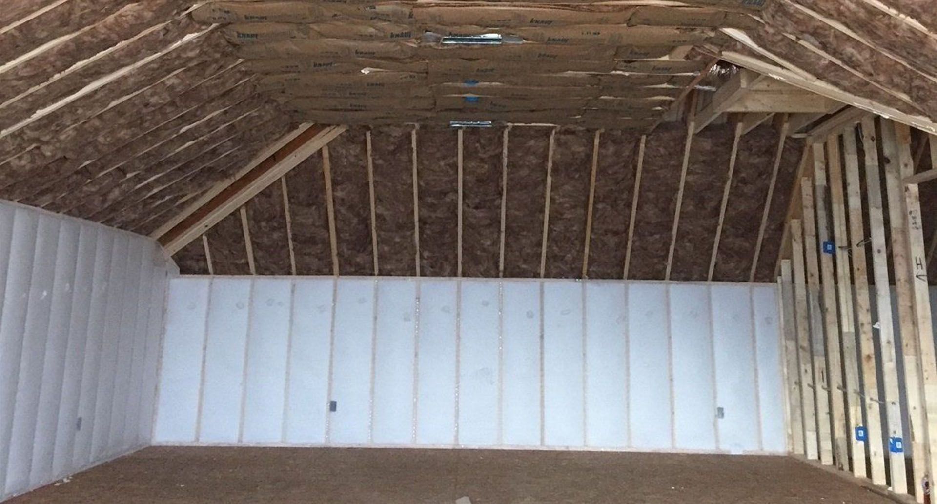 Empty attic with exposed wooden rafters and white paneled walls.
