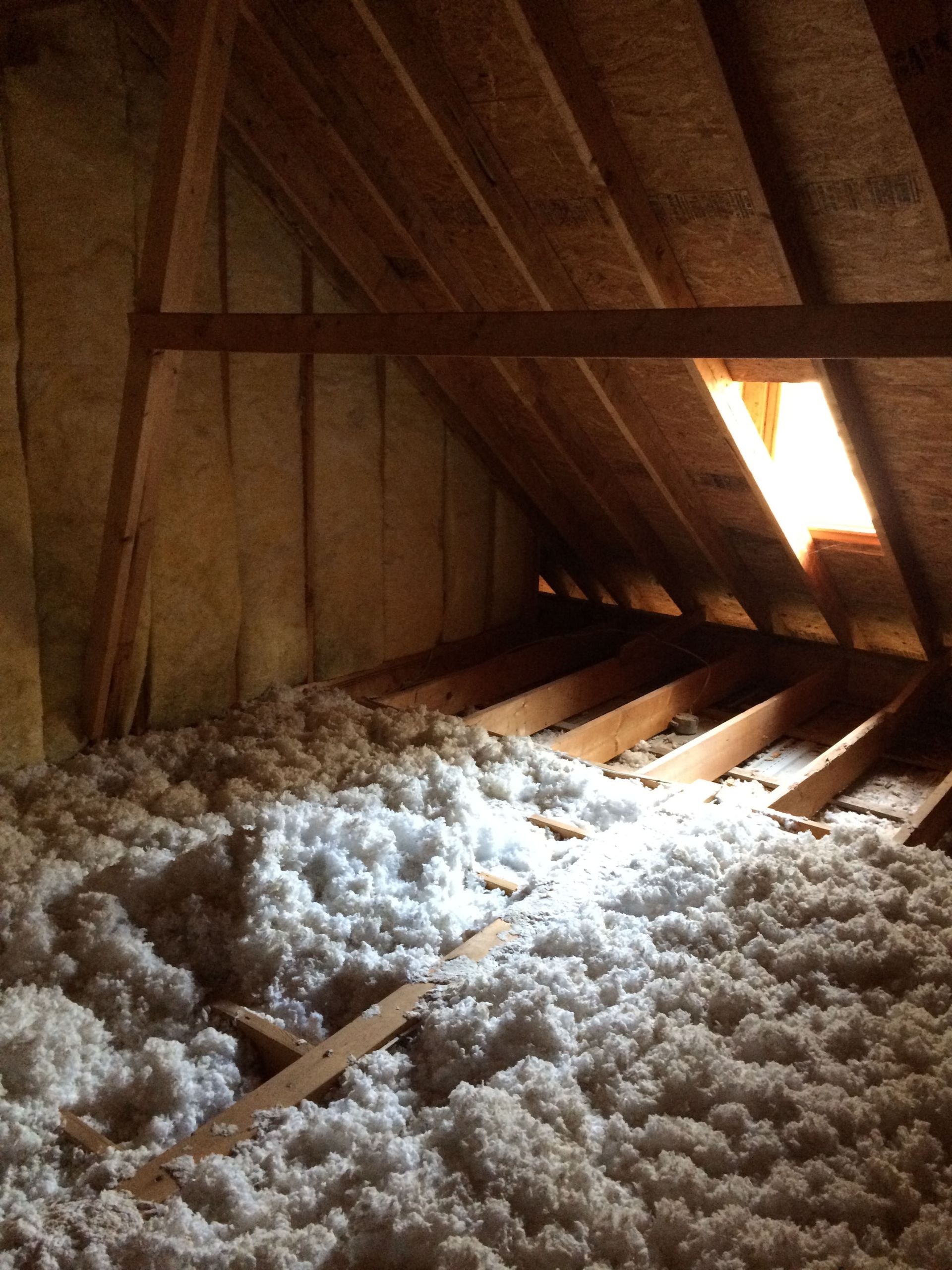 Attic with exposed wooden rafters and insulation, lit by sunlight through a roof opening