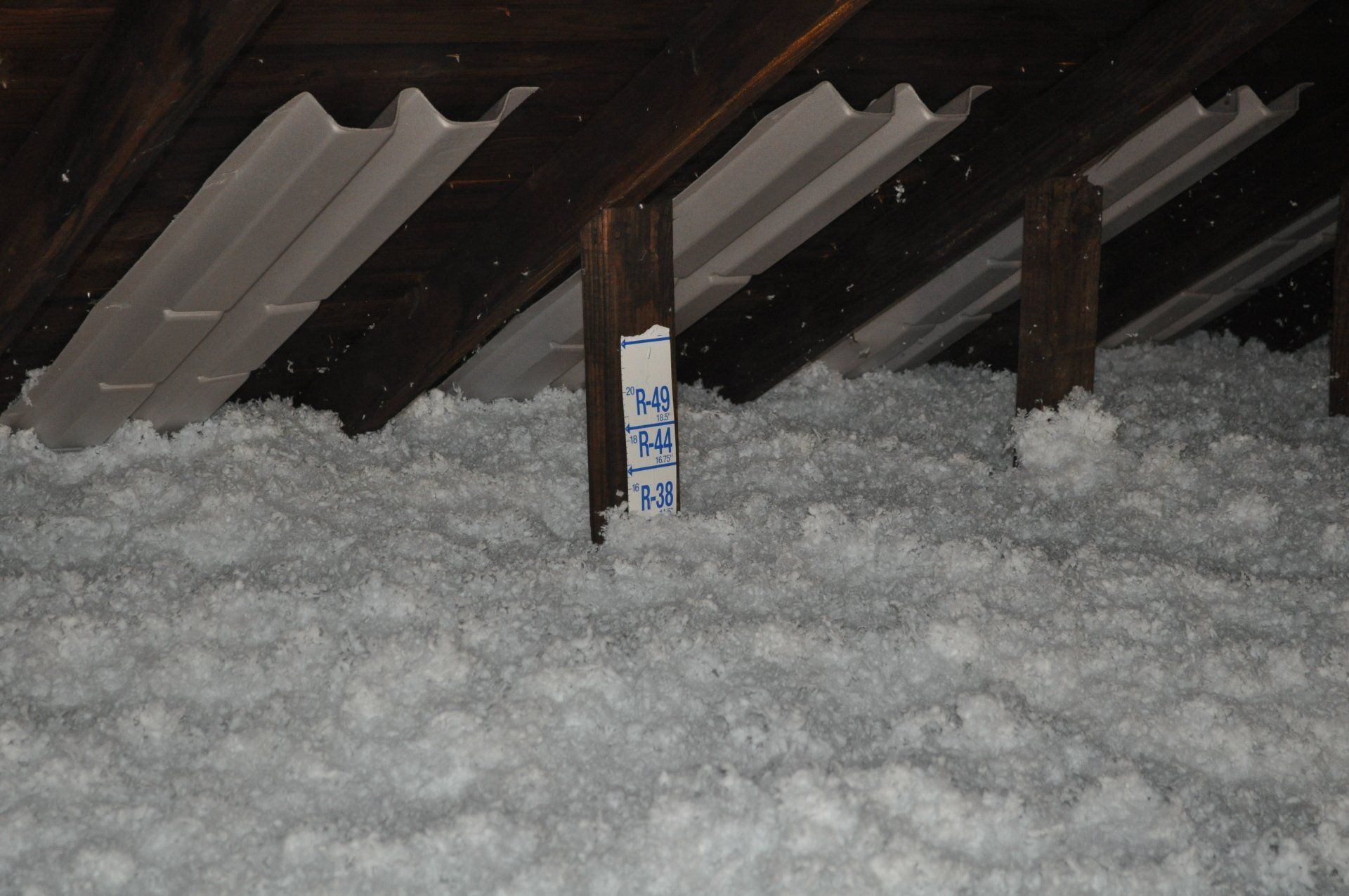Snow piled under roof beams with a small measuring stake in the center.