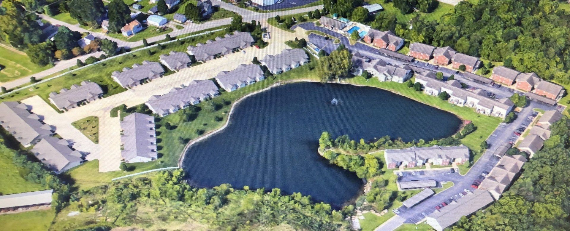 Aerial view of a suburban apartment complex with a central pond and surrounding trees