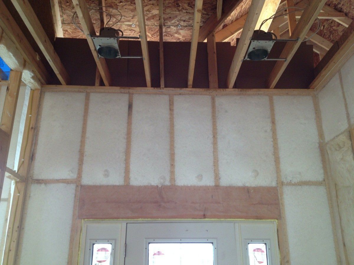 Interior wall under construction with exposed wooden ceiling joists and unfinished drywall framing.