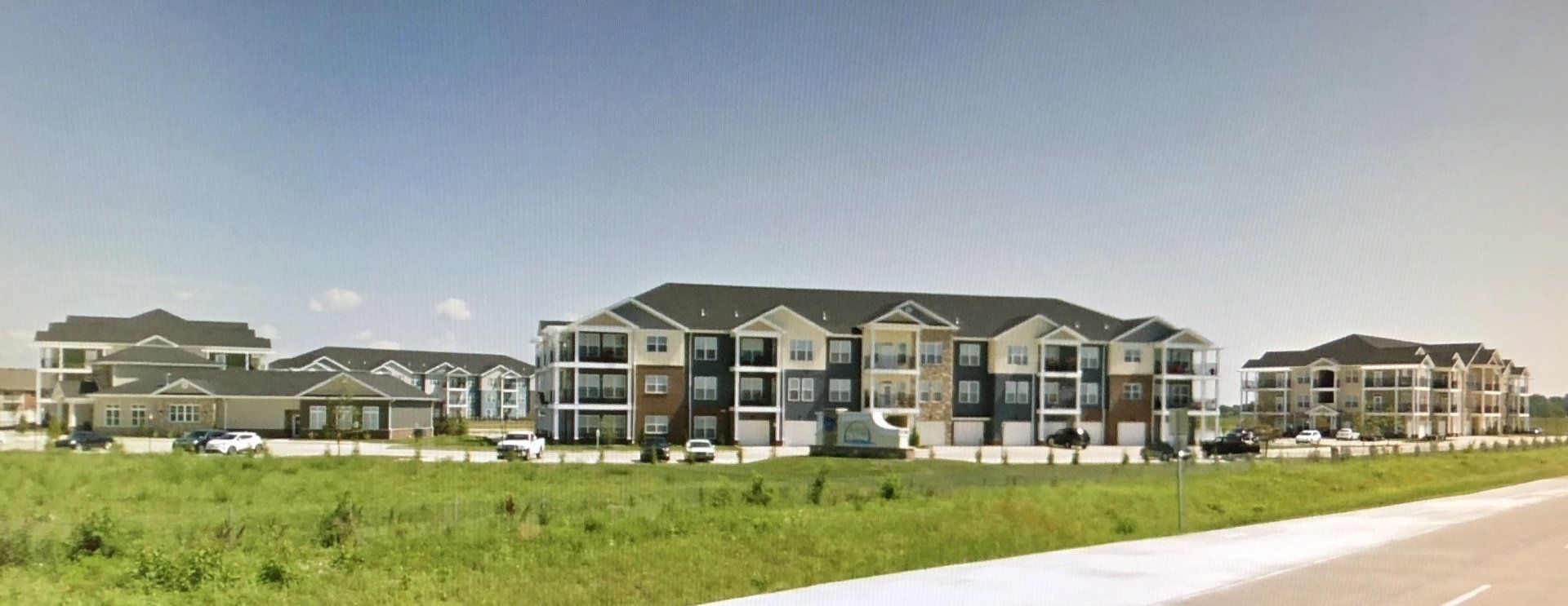 Modern apartment buildings across a grassy field under a clear sky
