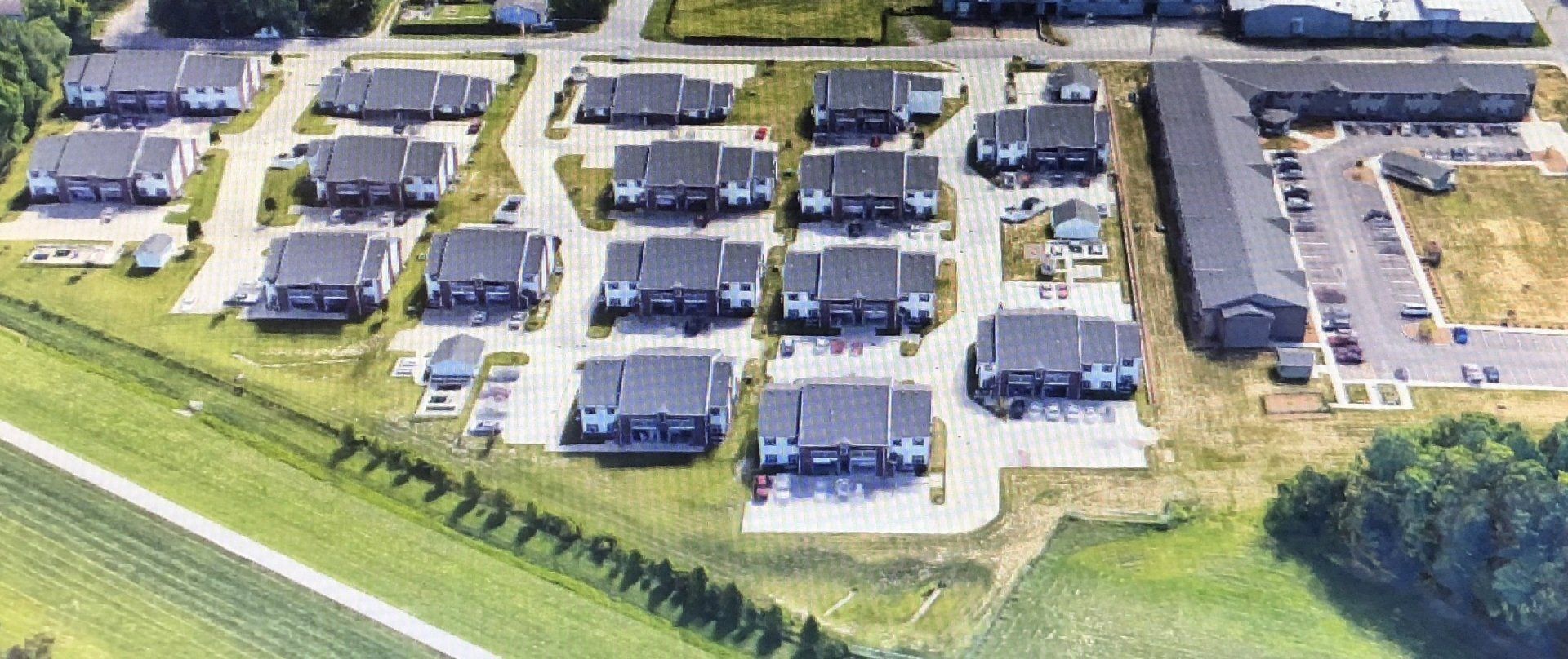 Aerial view of a suburban neighborhood with rows of houses, driveways, and parked cars.