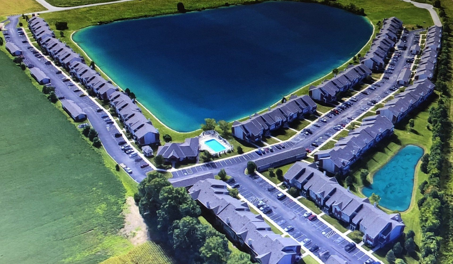 Aerial view of a suburban neighborhood around a large pond with houses, roads, and green lawns