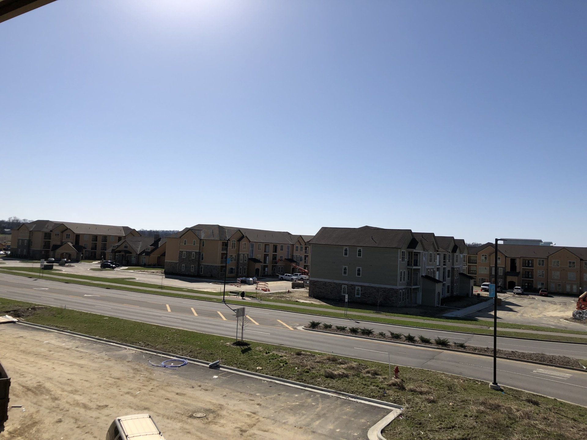 Suburban street with new houses, sidewalks, and open dirt lots under a clear blue sky