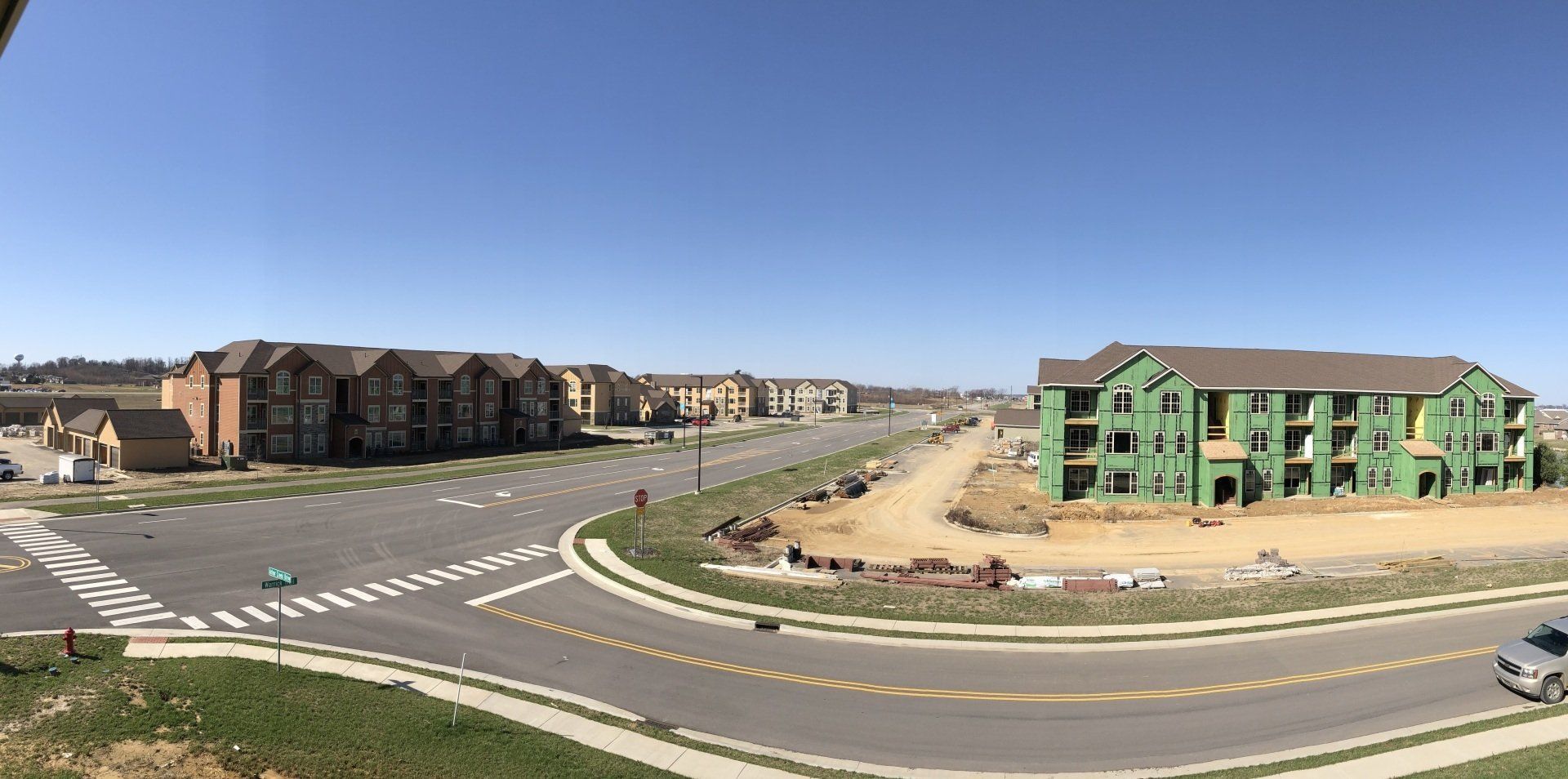 Suburban street scene with new apartment buildings and a wide road under a clear blue sky