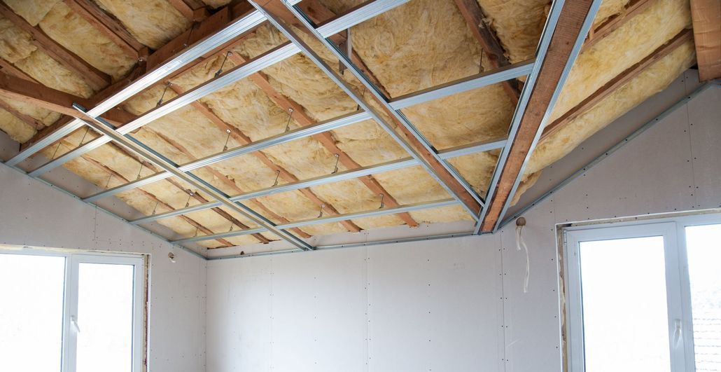 Interior room with exposed wooden ceiling framing and unfinished insulation above white walls and windows.