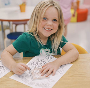 A group of young girls are sitting at a table drawing with pencils.