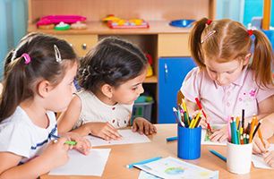 A group of young girls are sitting at a table drawing with pencils