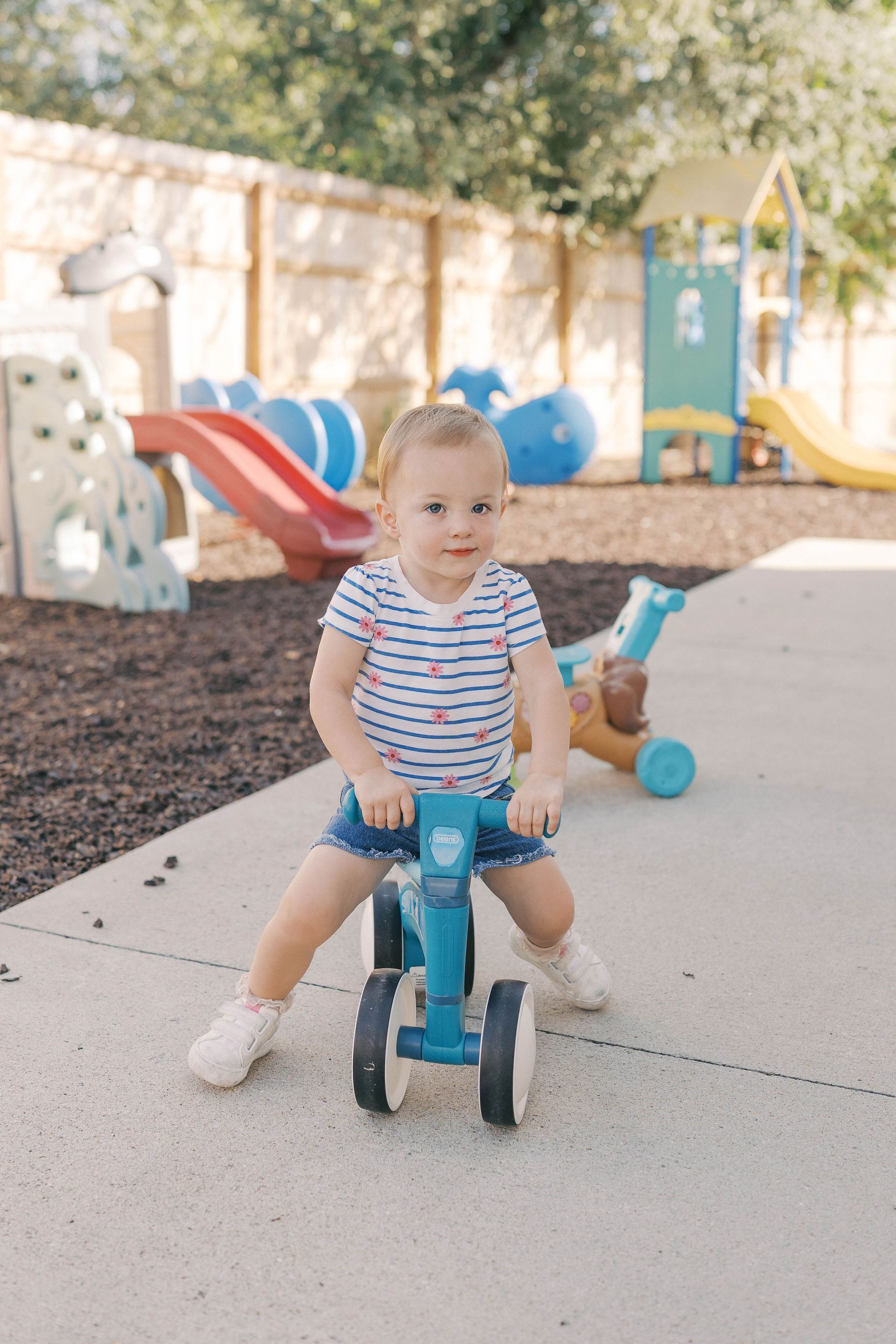 Child riding a blue balance bike on a paved area.