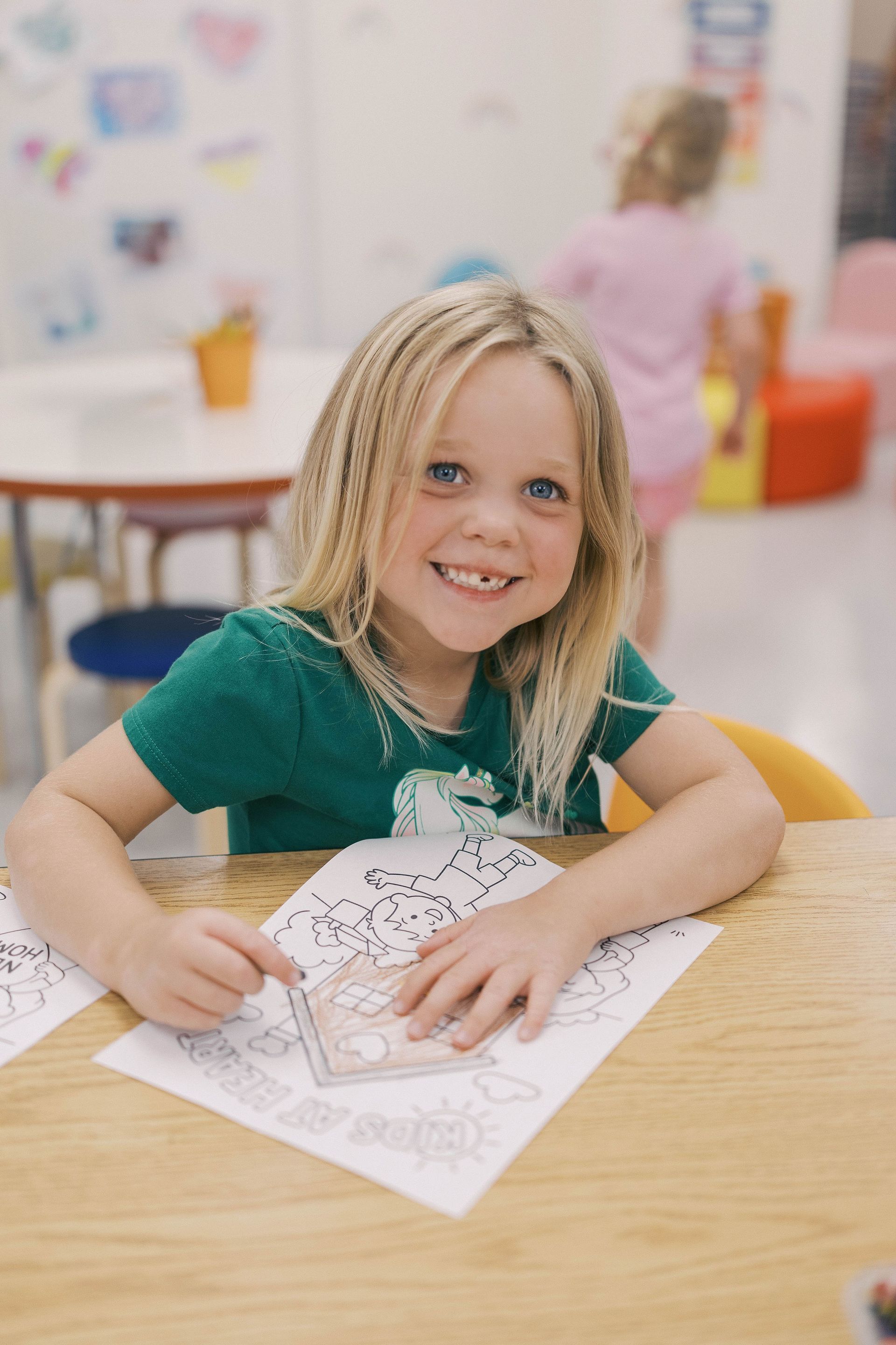 Girl smiling while coloring at a table in a classroom.