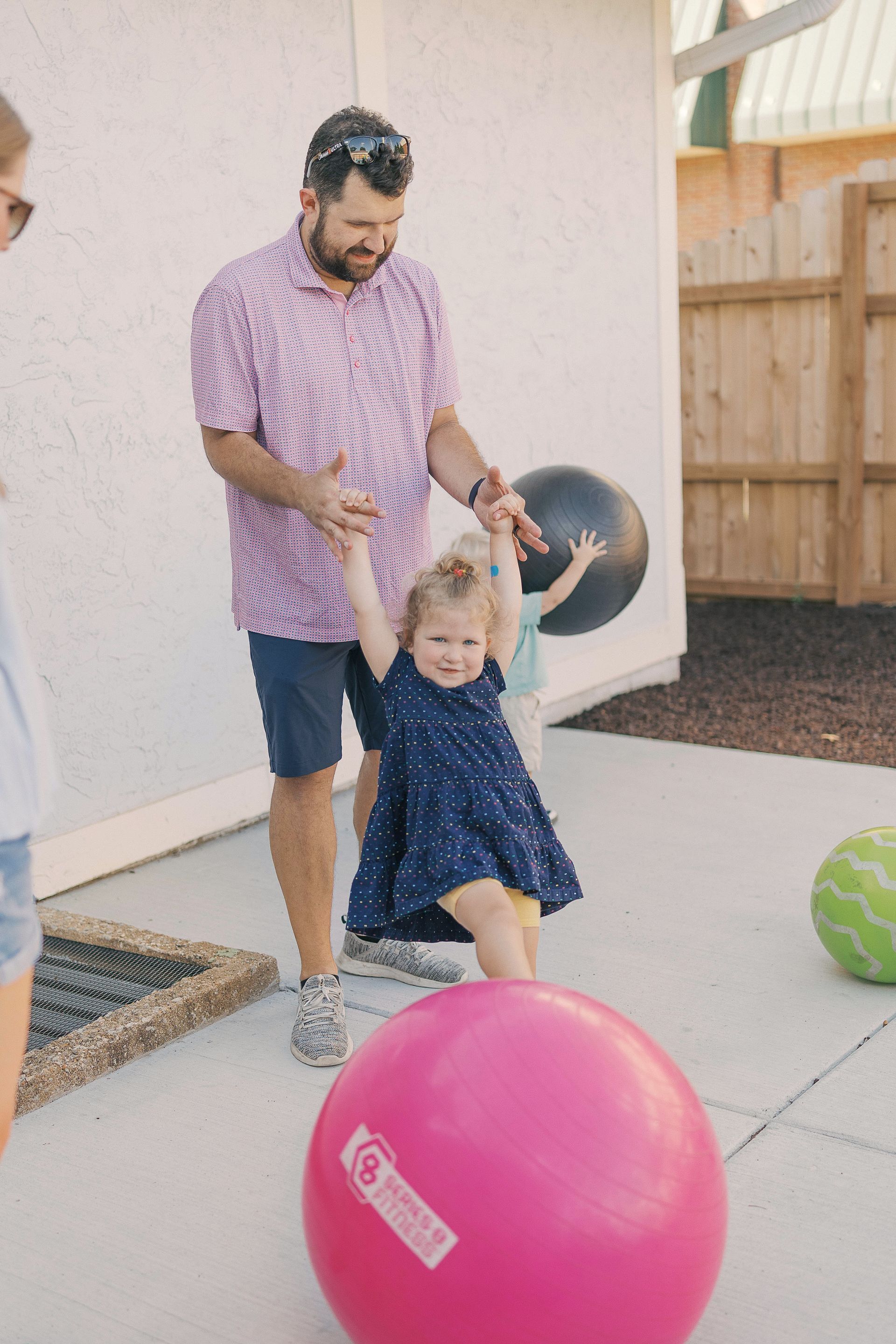 Man holding hands with a girl, swinging her over a large pink ball.