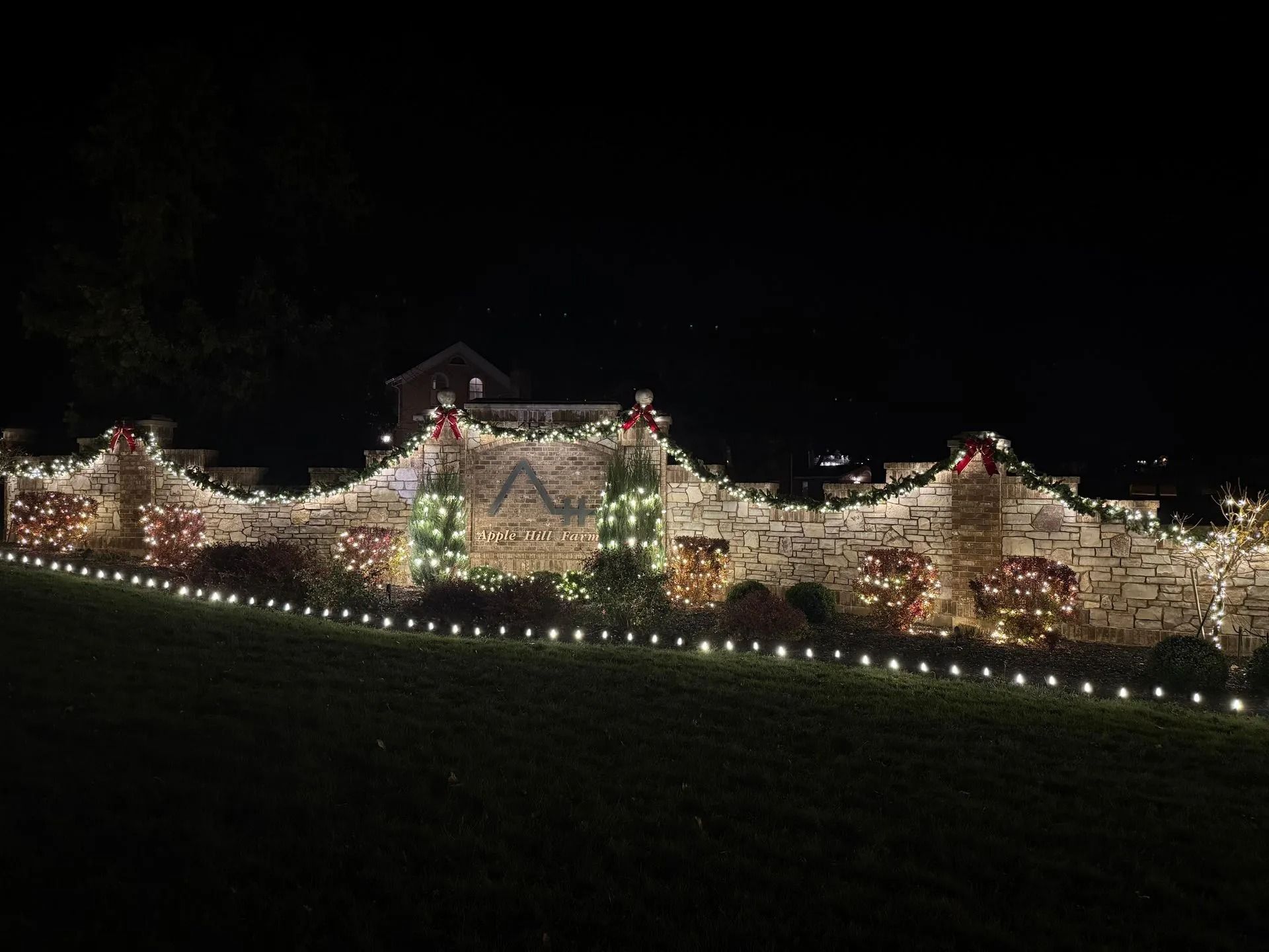 A long stone wall at night, illuminated with white Christmas lights and festive decorations.