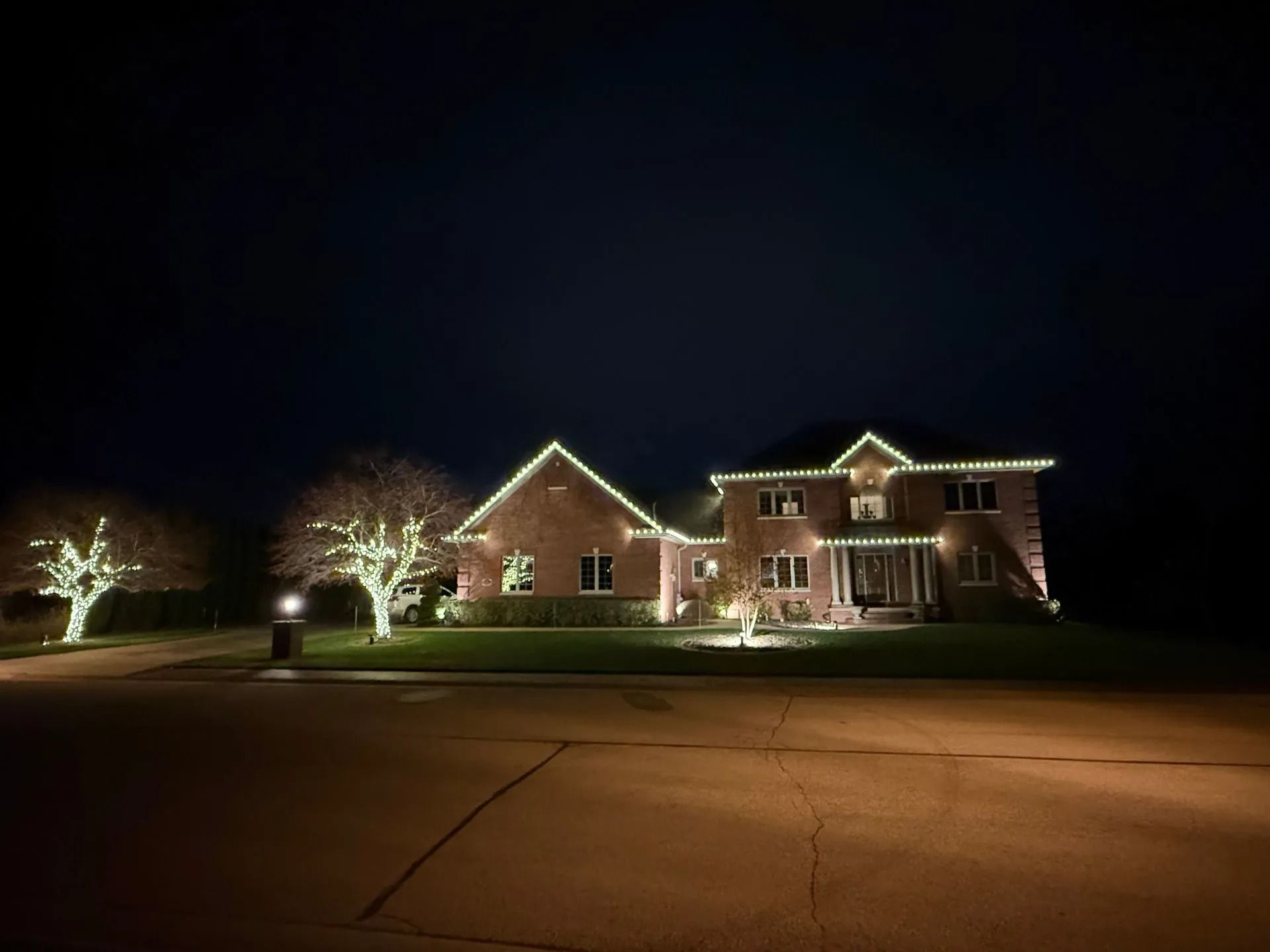 A house at night, illuminated with white lights around the roofline and trees.