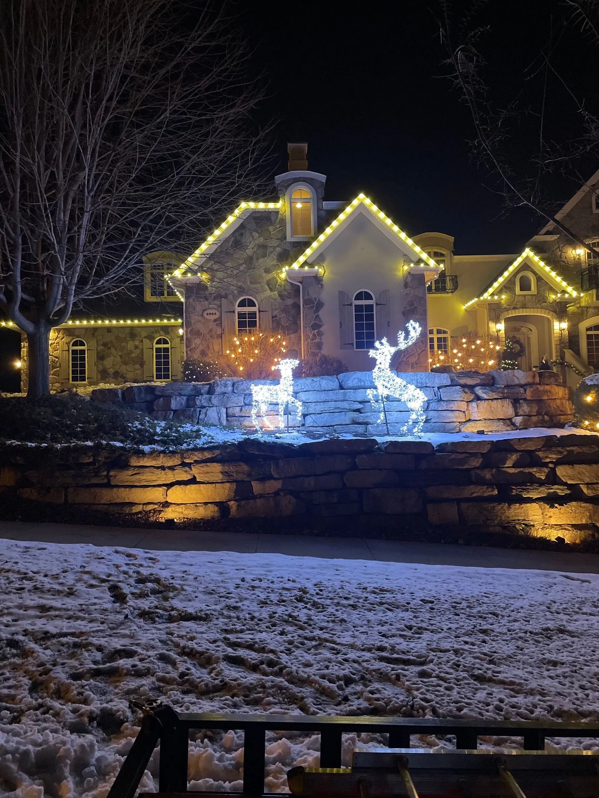 House decorated with white lights and illuminated reindeer on a snowy night.