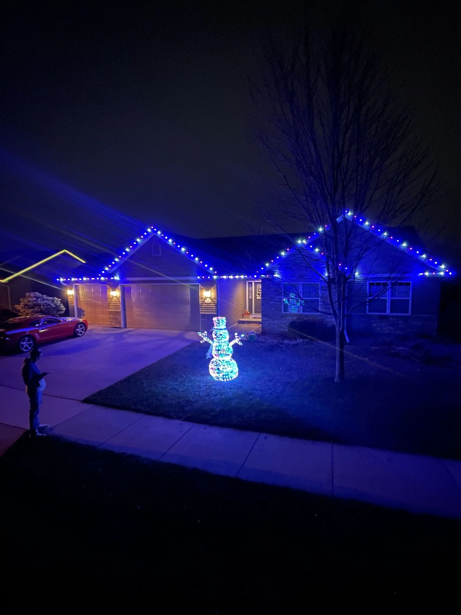 A house decorated with blue Christmas lights and a snowman, lit at night.