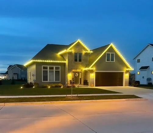 House with yellow lights outlining the roof, windows, and bushes at dusk.