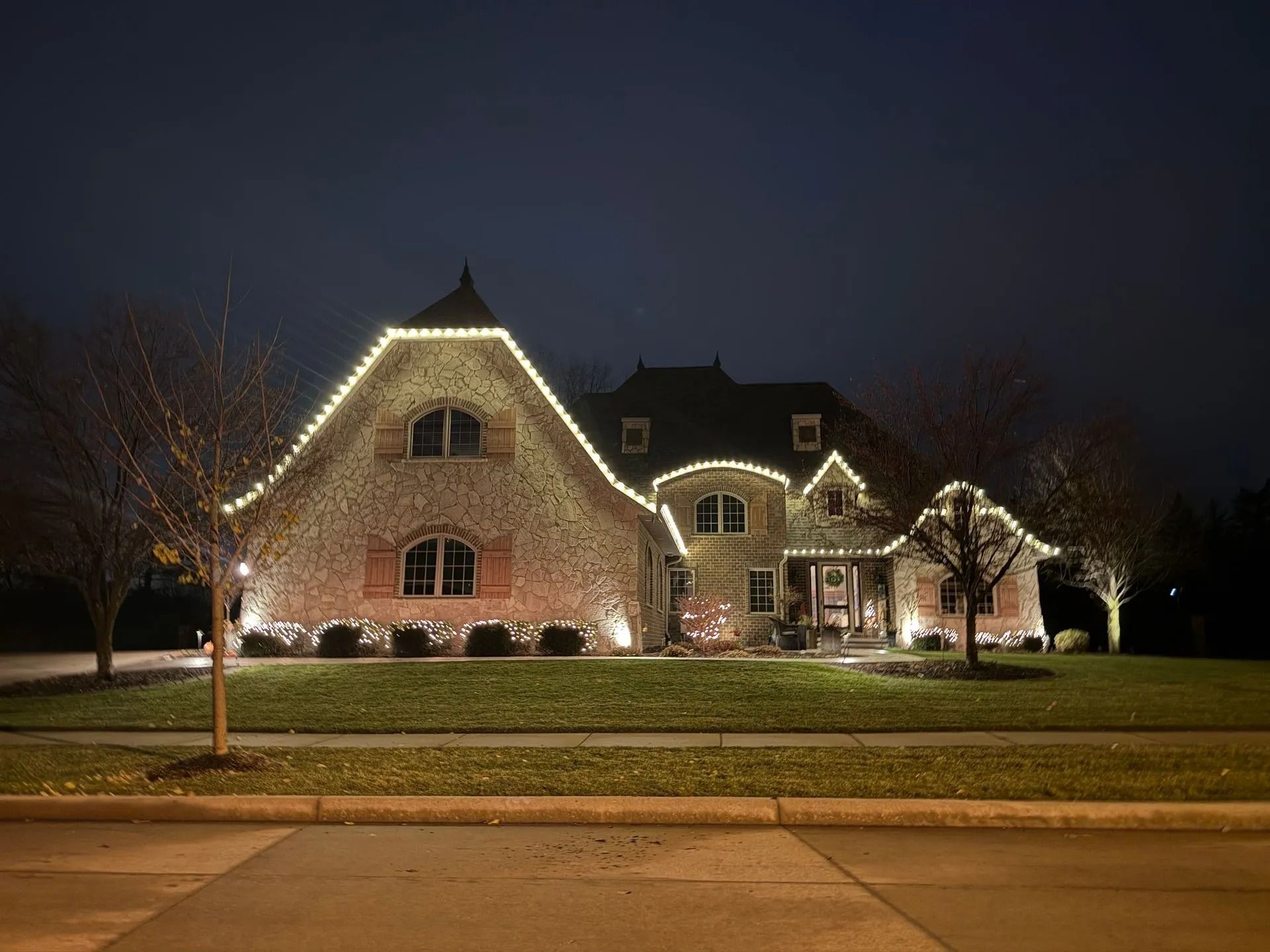 House at night with roof and yard outlined with white Christmas lights.