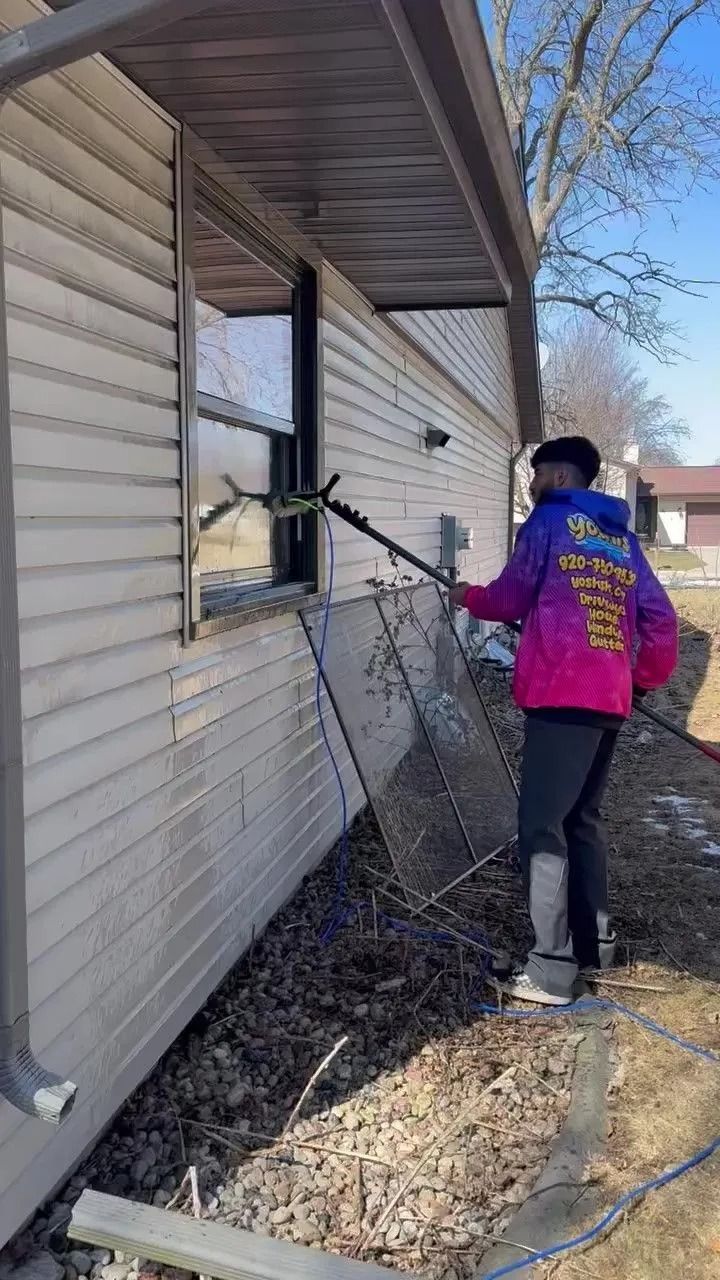 Person washes a window on the side of a house with a long-handled tool on a sunny day.