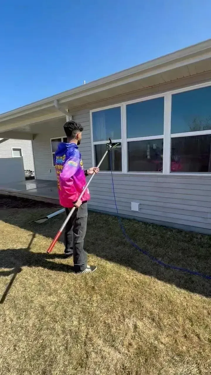 Person washing a window with a long-handled tool outside a house on a sunny day.