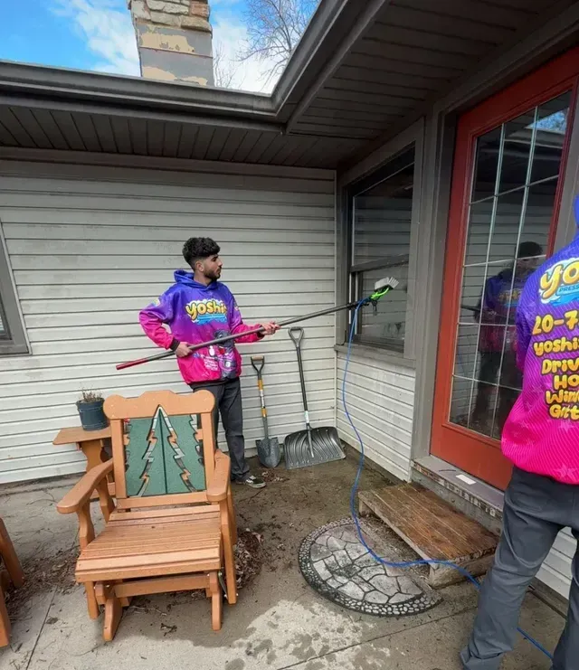 Two people washing a window of a house. One is holding a pole, the other is reflected. Outside setting.