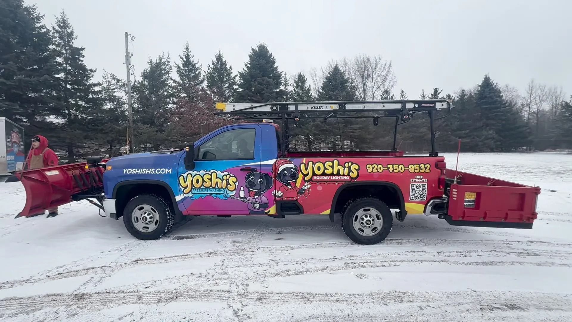 Truck with snowplow and Yoshi's logo plowing snow, outdoors.