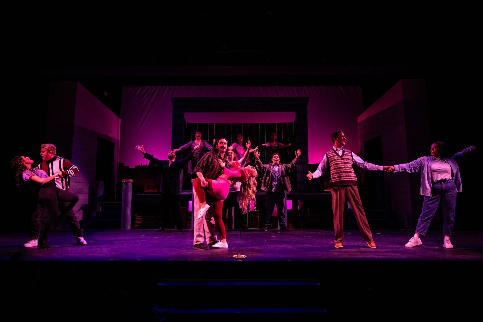 A group of people are dancing on a stage with purple lights.